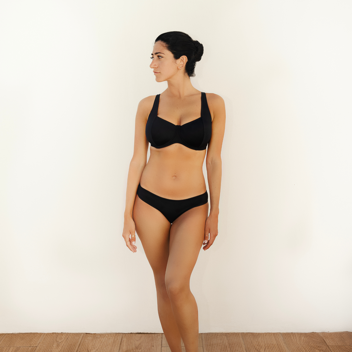 Black Balconette Shaped Swimwear snug bikini  top and classic bikini briefs worn by greek model looking at the side on a white backgrond